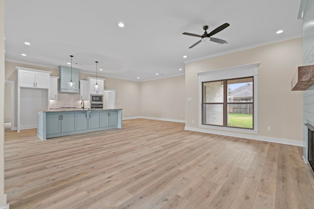 unfurnished living room featuring ornamental molding, a large fireplace, ceiling fan, and light hardwood / wood-style floors