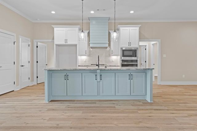 kitchen with decorative light fixtures, built in microwave, white cabinets, a kitchen island with sink, and stainless steel oven