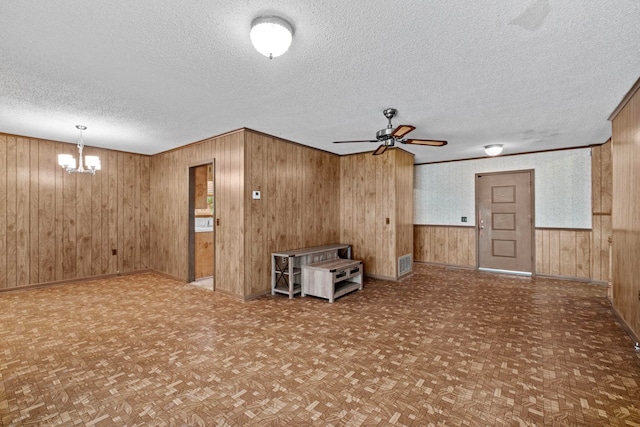 unfurnished living room with parquet flooring, wooden walls, ceiling fan with notable chandelier, and a textured ceiling