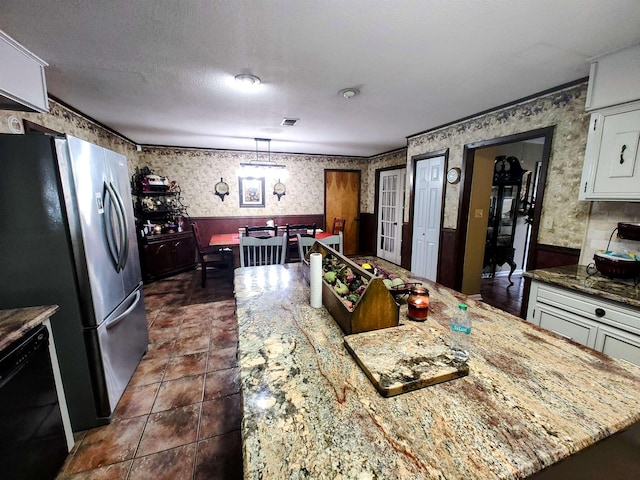 kitchen featuring white cabinetry, hanging light fixtures, stainless steel refrigerator, black dishwasher, and a kitchen island