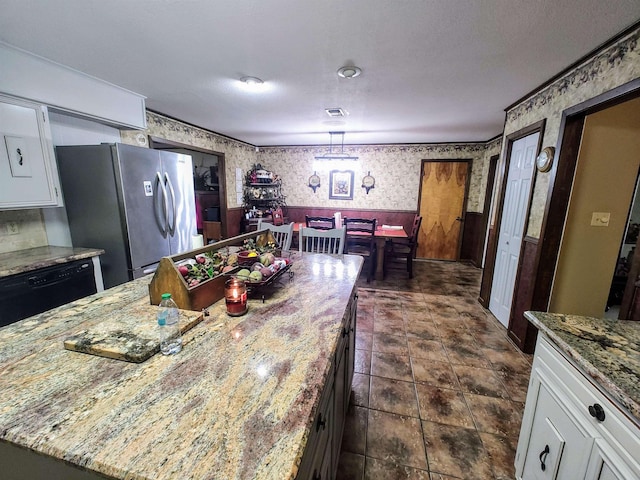 kitchen with hanging light fixtures, stainless steel refrigerator, a kitchen island, light stone countertops, and white cabinets