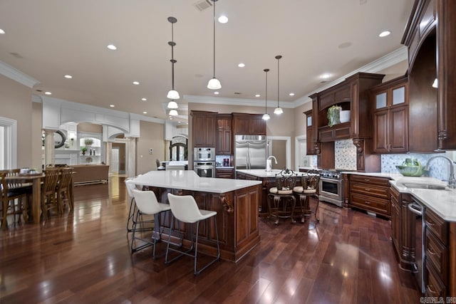 kitchen featuring sink, ornate columns, high end appliances, decorative light fixtures, and a large island