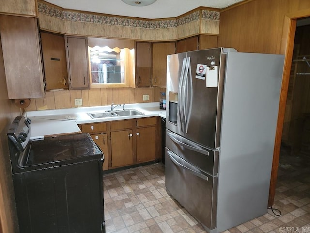 kitchen featuring sink, black range, wooden walls, and stainless steel refrigerator with ice dispenser