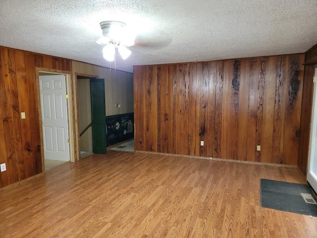 unfurnished room featuring ceiling fan, wooden walls, light hardwood / wood-style floors, and a textured ceiling