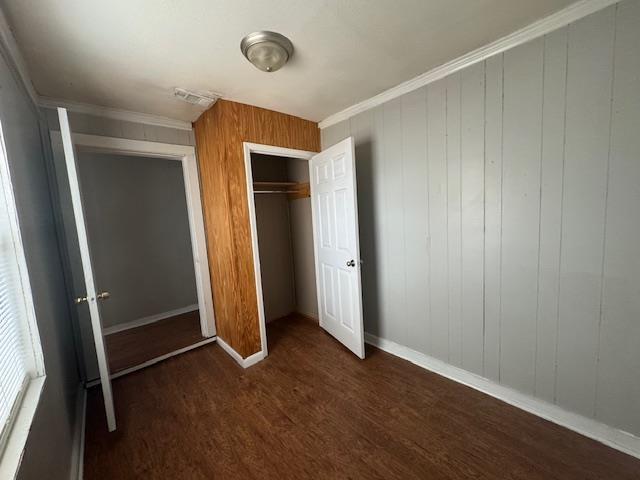 unfurnished bedroom with a closet, ornamental molding, and dark hardwood / wood-style floors