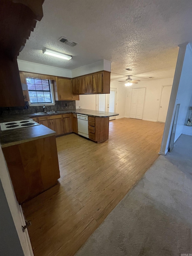 kitchen featuring stovetop, sink, white dishwasher, kitchen peninsula, and light wood-type flooring