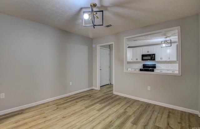 kitchen with hanging light fixtures, tasteful backsplash, black appliances, white cabinets, and light wood-type flooring