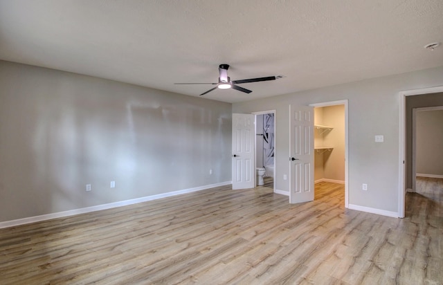 unfurnished bedroom with a walk in closet, a textured ceiling, a closet, ceiling fan, and light hardwood / wood-style floors