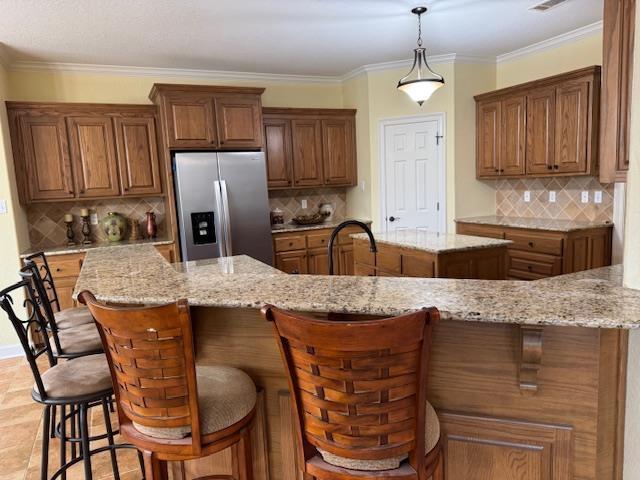 kitchen with a kitchen bar, stainless steel fridge, light stone countertops, and a kitchen island