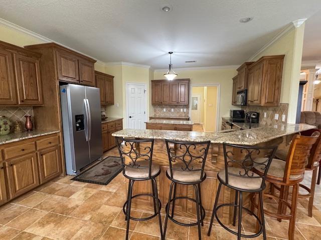 kitchen featuring pendant lighting, stainless steel fridge, a kitchen bar, light stone counters, and kitchen peninsula