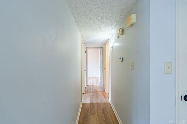 hallway with a textured ceiling and light hardwood / wood-style floors