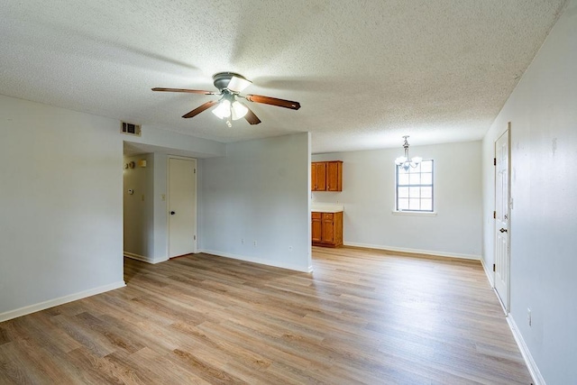 empty room featuring ceiling fan with notable chandelier, light hardwood / wood-style floors, and a textured ceiling