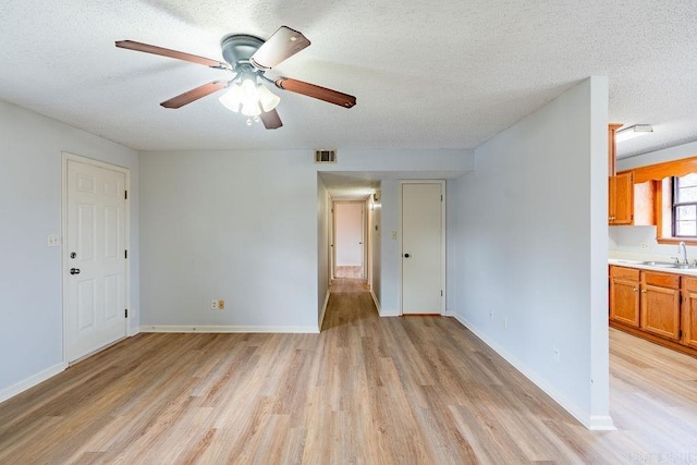 empty room featuring ceiling fan, sink, a textured ceiling, and light wood-type flooring