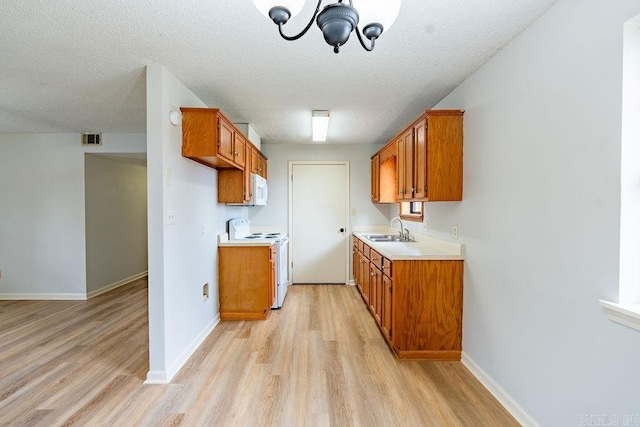 kitchen with white appliances, sink, a textured ceiling, and light wood-type flooring