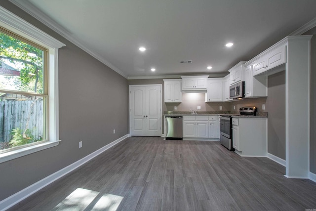 kitchen featuring a healthy amount of sunlight, ornamental molding, stainless steel appliances, and white cabinets