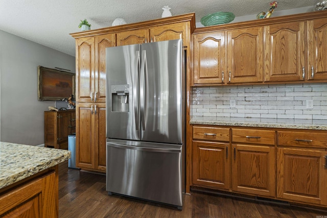 kitchen with dark hardwood / wood-style floors, stainless steel refrigerator with ice dispenser, tasteful backsplash, light stone countertops, and a textured ceiling