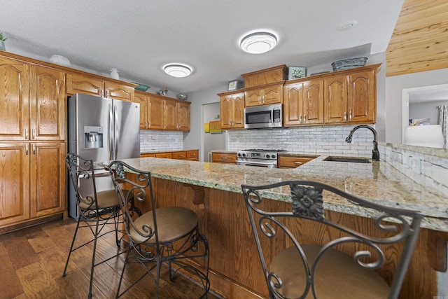 kitchen featuring sink, a kitchen breakfast bar, stainless steel appliances, light stone countertops, and kitchen peninsula