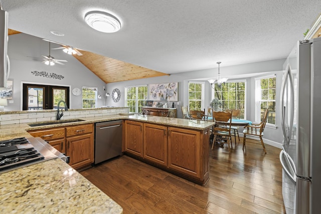 kitchen featuring lofted ceiling, sink, appliances with stainless steel finishes, light stone counters, and kitchen peninsula