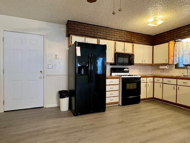 kitchen featuring light hardwood / wood-style flooring, white cabinets, a textured ceiling, and black appliances