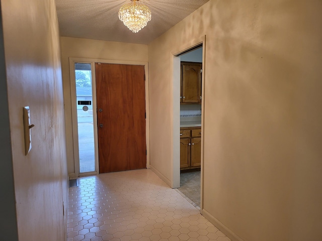 hall featuring light tile patterned flooring, a textured ceiling, and a notable chandelier