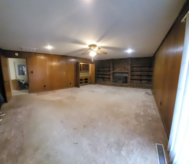 unfurnished living room with ceiling fan, wooden walls, and light carpet