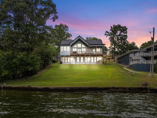 back house at dusk with a water view and a yard