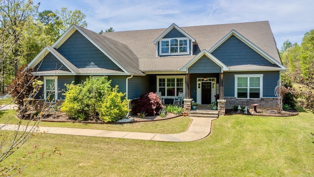 craftsman house featuring a front yard, a shingled roof, stone siding, and covered porch