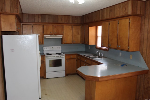 kitchen with sink, white appliances, a textured ceiling, kitchen peninsula, and wood walls