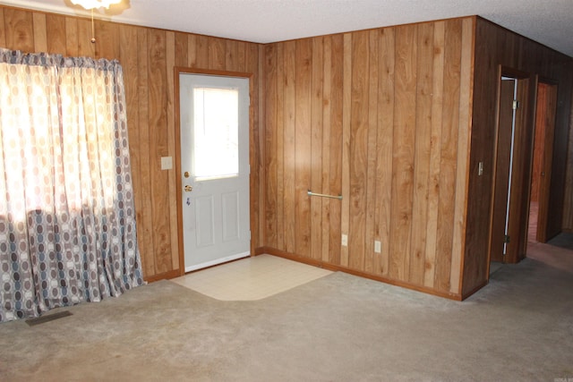 foyer with a textured ceiling, light carpet, and wood walls