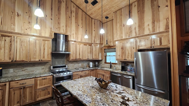 kitchen featuring wall chimney range hood, sink, appliances with stainless steel finishes, light stone counters, and decorative light fixtures