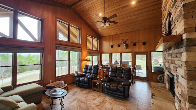 living room featuring high vaulted ceiling, wooden walls, a fireplace, ceiling fan, and wood ceiling