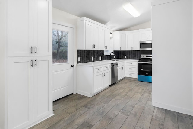 kitchen featuring lofted ceiling, sink, tasteful backsplash, stainless steel appliances, and white cabinets