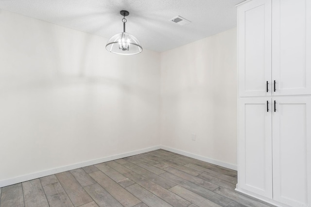 empty room featuring an inviting chandelier, light hardwood / wood-style floors, and a textured ceiling