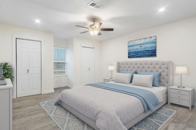 bedroom with ceiling fan, two closets, and light hardwood / wood-style floors