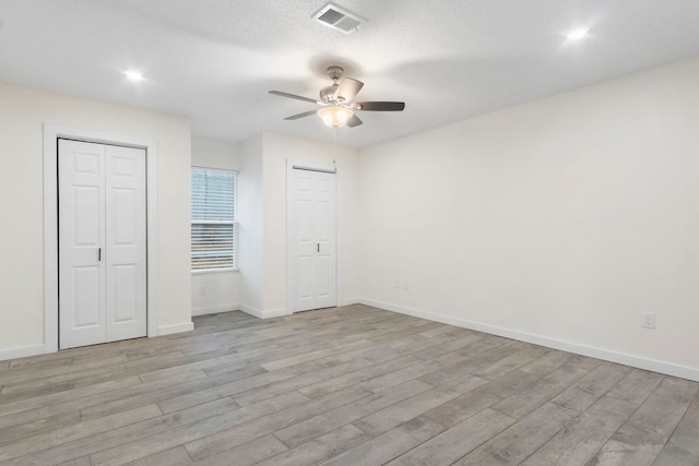 unfurnished bedroom with two closets, light hardwood / wood-style floors, ceiling fan, and a textured ceiling