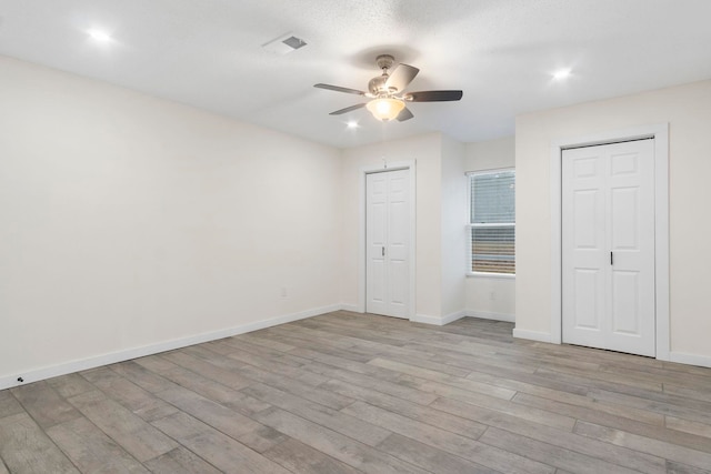 unfurnished bedroom featuring ceiling fan, multiple closets, and light wood-type flooring