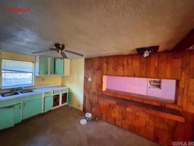 kitchen featuring sink, wooden walls, a textured ceiling, and ceiling fan