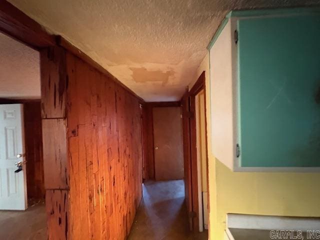 hallway featuring a textured ceiling and wood walls