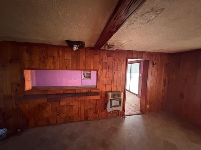 interior space featuring heating unit, a textured ceiling, wooden walls, and beamed ceiling