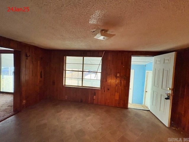 spare room featuring wooden walls and a textured ceiling