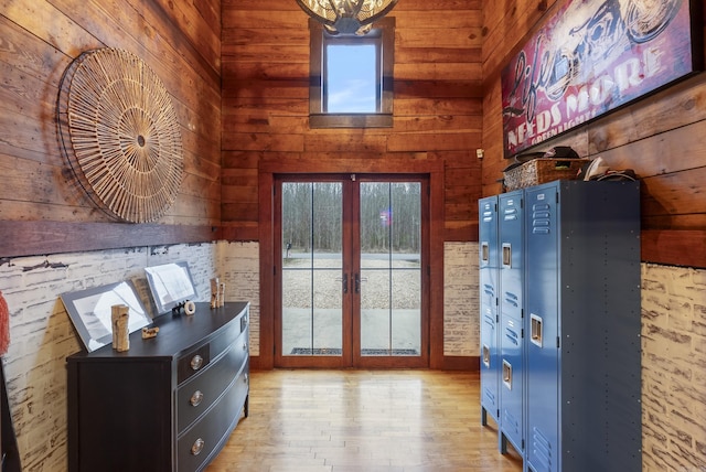 doorway with french doors, a towering ceiling, wooden walls, and light hardwood / wood-style floors