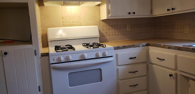 kitchen featuring white gas range oven, extractor fan, white cabinets, decorative backsplash, and tile countertops