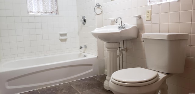 bathroom with tile walls, tiled shower / bath, tile patterned flooring, and toilet