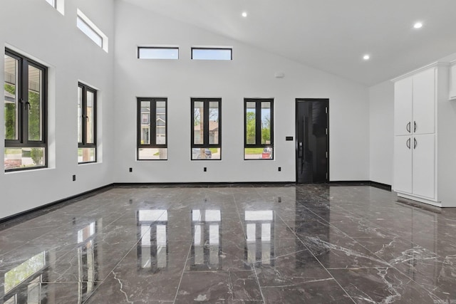 empty room with high vaulted ceiling, plenty of natural light, marble finish floor, and recessed lighting