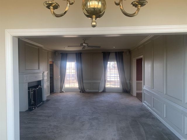 unfurnished living room featuring ornamental molding, ceiling fan, and dark carpet