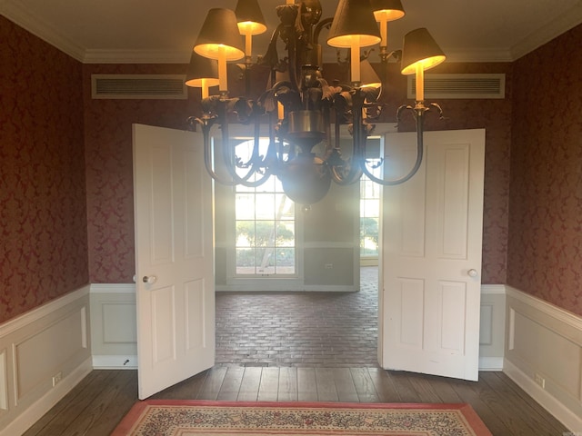 unfurnished dining area with crown molding, an inviting chandelier, and dark hardwood / wood-style flooring