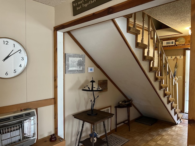 stairs with heating unit, parquet floors, and a textured ceiling