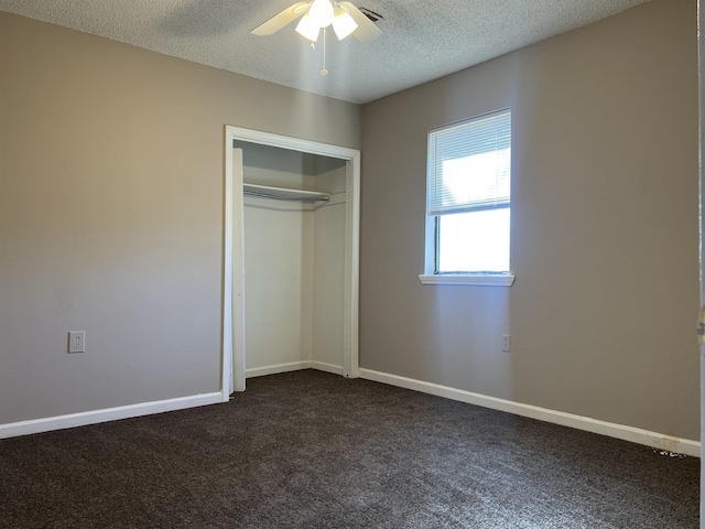 unfurnished bedroom with ceiling fan, a textured ceiling, dark carpet, and a closet