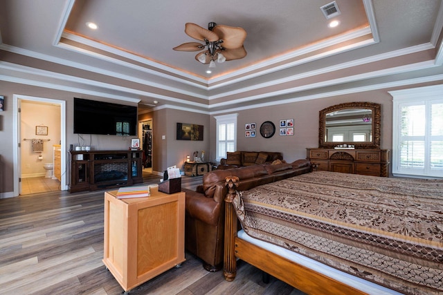 bedroom featuring multiple windows, ensuite bathroom, hardwood / wood-style floors, and a tray ceiling