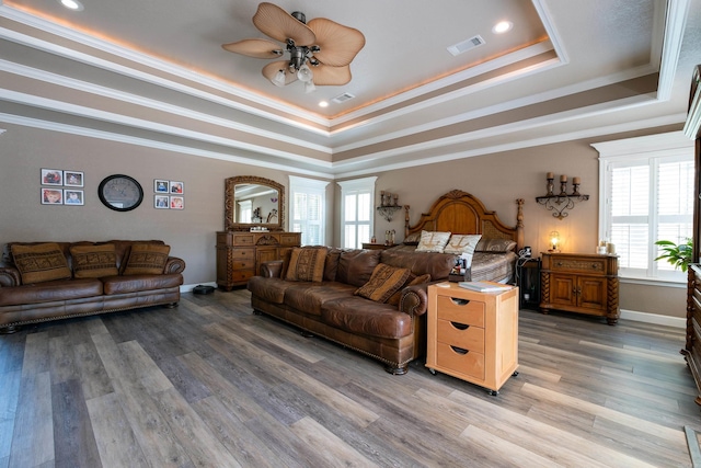 bedroom featuring ornamental molding, a tray ceiling, hardwood / wood-style floors, and multiple windows